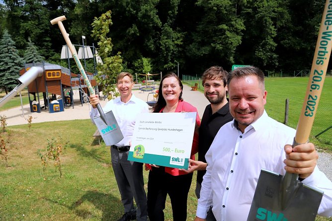 B&uuml;rgermeister Christian Zwingmann, Klimaschutzmanager Stephan Gunkel, SWL-Gesch&auml;ftsf&uuml;hrerin Evelyn Rudolph und ihr Kollege R&uuml;diger Steinberg (von rechts) bei der symbolischen &Uuml;bergabe des Spendenschecks auf dem Hundeshagener Spielplatz. Die B&auml;ume und Str&auml;ucher im Hintergrund hatte der st&auml;dtische Bauhof bereits im Vorfeld gepflanzt.  (Foto: Ren&eacute; Wei&szlig;bach)